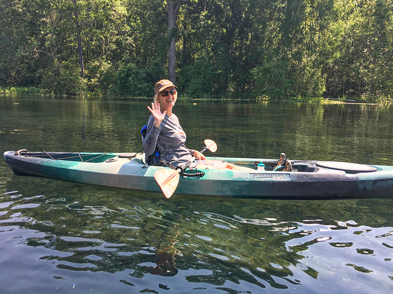 A woman in a kayak, waving at the camera.